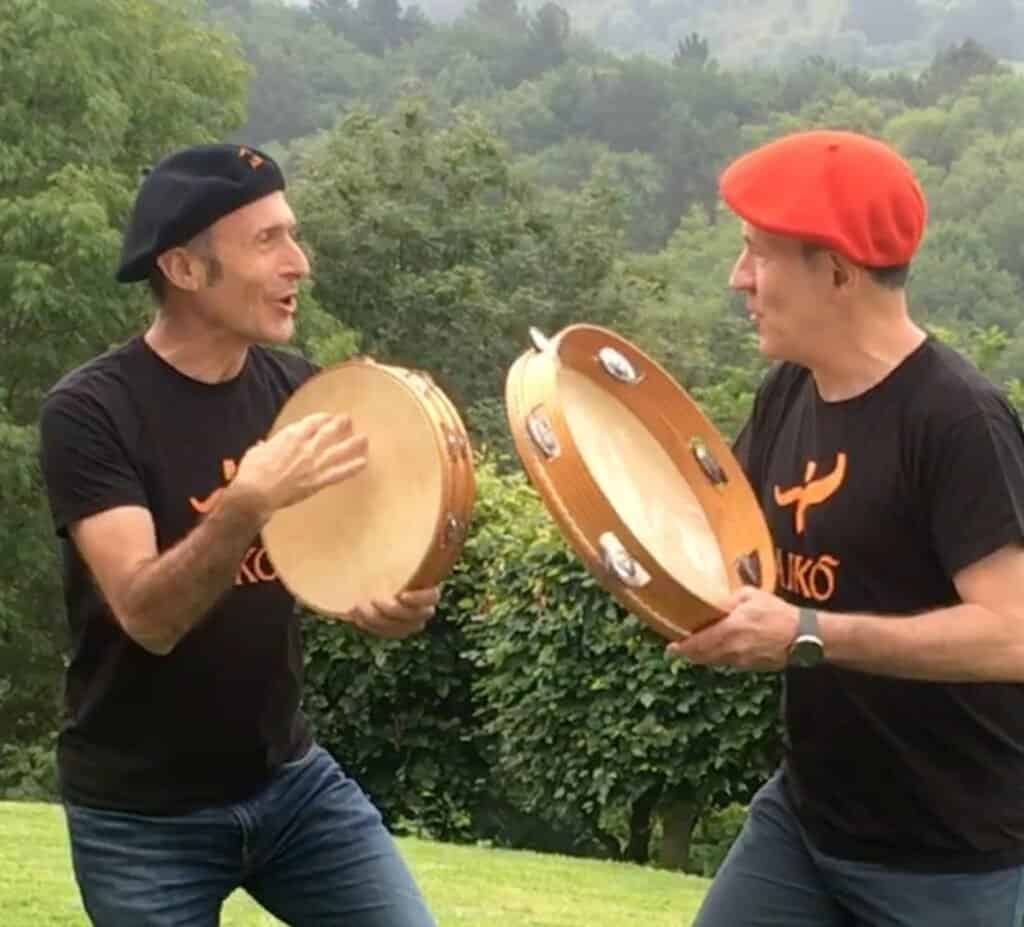 Hombres tocando panderetas en un paisaje natural.